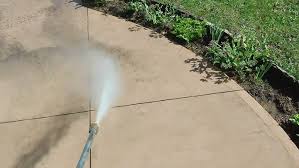 High-velocity pressure washing stream stripping deep dark grease from aged local concrete slabs